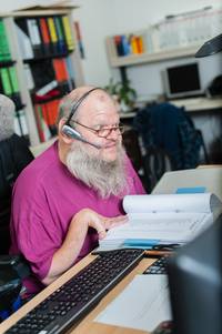 Günther mit Headset liest ein Buch neben dem Computer Keyboard